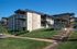 Scenic view of a charming apartment building with balconies and well-manicured green lawns under a blue sky.
