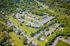 Aerial view of a sprawling apartment complex surrounded by lush greenery with a central pool, tennis court, and ample parking.