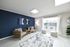 Bright living room with stylish decor, featuring a navy accent wall, modern seating, and large window overlooking a pool.