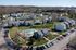 Charming aerial view of a contemporary apartment complex with lush green lawns, a refreshing swimming pool, and ample parking, nestled in a tranquil suburban setting.