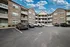 Charming three-story apartment complex with brick facade and spacious balconies, showcasing convenient parking and a welcoming atmosphere under a bright blue sky.
