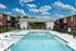 Charming outdoor pool area with sun loungers and umbrellas, surrounded by modern brick apartment buildings under a vibrant sky.