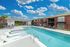 Inviting community pool area with modern lounge chairs, surrounded by brick buildings and a vibrant blue sky.