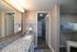 Elegant bathroom with a granite countertop, large mirror, and towel racks, leading to a modern shower area and adjacent closet space with stylish shelving.