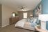 Elegant bedroom with modern decor, featuring a plush bed with stylish pillows, a wooden dresser with a round mirror, and calming blue accent wall.