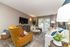 Elegant living room with modern decor, featuring a plush mustard armchair, stylish sofa, chic coffee table, and large windows with natural light.