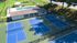 Vibrant aerial view of a community recreation area featuring multiple blue tennis courts and a sparkling swimming pool with lounge seating, surrounded by lush greenery.