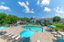 Inviting apartment community with a sparkling outdoor pool, relaxing sun loungers, and vibrant blue umbrellas under a clear sky.