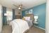 Inviting bedroom with soothing teal accent wall, modern ceiling fan, cozy bed with plush pillows, and elegant decor for a relaxing ambience.