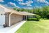 Charming brick house with lush green lawn, vibrant flowers, and a sunny blue sky backdrop.
