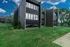 Contemporary apartment building with sleek dark facade, framed by lush green landscaping and bright blue sky.