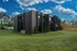 Contemporary apartment building with sleek black exterior, surrounded by lush green lawns and vibrant landscaping under a bright blue sky.