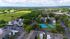 Aerial view of a serene apartment complex surrounded by lush greenery, featuring ample parking and vibrant tennis courts.