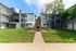Charming apartment complex exterior featuring modern architecture with a central stone fireplace, surrounded by lush green lawns and trees.
