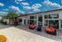 Vibrant outdoor patio area with modern seating and large glass doors under a bright blue sky with fluffy clouds.