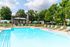 Inviting apartment complex pool with lush greenery, sun loungers, and shaded seating areas under a clear blue sky.