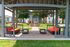 Charming outdoor pavilion with vibrant orange-cushioned seating, perfect for relaxation and entertaining, featuring a modern grill station amidst lush green surroundings.