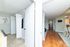Inviting apartment hallway with wooden flooring and a cozy carpeted room, complemented by modern decor and ample natural light.