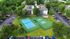 Aerial view of a vibrant apartment complex featuring well-maintained tennis courts surrounded by lush greenery and ample parking.