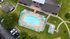 Charming aerial view of a refreshing pool with blue umbrellas and sun loungers, surrounded by lush green grass and cozy residential buildings.