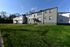 Charming apartment building with spacious green lawn and modern gray facade, basking in the morning sunlight.