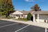 Charming brick office building with lush landscaping, accessible parking, and convenient mailboxes, under a bright blue sky.