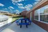 Charming outdoor patio with a sleek grill, vibrant blue picnic table, and lush green lawn under a picturesque sky.