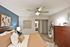 Inviting bedroom with modern decor, featuring a plush, stylish bed, contemporary art, elegant wooden dresser, and soothing blue accent wall.