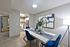Modern dining area featuring a sleek table with blue chairs, contemporary art, and an inviting kitchen in the background, perfect for entertaining.