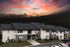 Charming apartment complex under a vibrant sunset sky, featuring modern two-story buildings with balconies and lush greenery.