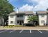 Charming two-story apartment building with a welcoming porch, surrounded by lush greenery and vibrant flower beds, offering an appealing suburban vibe.