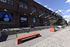 Charming urban streetscape with brick facade and colorful murals, featuring outdoor seating and vibrant planters.