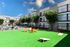 Vibrant apartment complex exterior showcasing lush green courtyard, cozy seating area, and sunlit balconies under a clear blue sky.