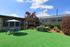 Charming outdoor patio with a barbecue grill, table set with umbrella, and lush green turf, ideal for leisurely gatherings.