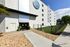 Modern apartment entrance with stylish landscaping, sleek white exterior, and inviting greenery.