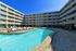 Luxurious apartment complex featuring a sparkling outdoor pool and stylish lounge area under clear blue sky.