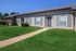 Charming single-story apartment with elegant shutters and lush green lawn, offering a welcoming and serene atmosphere.