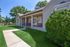 Charming single-story home with a welcoming porch, surrounded by lush greenery and a manicured lawn.