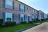 Charming brick apartment building with colonial-style architecture, featuring well-maintained landscaping and large windows, perfect for a cozy living environment.