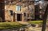 Charming apartment building with classic brick facade surrounded by lush greenery and shaded pathway.