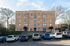 Charming brick apartment building with a clean, well-maintained facade, ample parking, and surrounded by lush greenery.