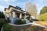 Charming two-story house with a spacious front porch, nestled amidst lush greenery and a well-maintained garden path.