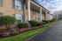 Charming brick apartment building with elegant columns and vibrant landscaped gardens under a blue sky.