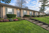 Charming brick apartment with inviting front landscaping, featuring vibrant flowers and a well-maintained lawn, under a clear blue sky.