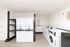 Bright and modern apartment laundry room featuring multiple washers and dryers, sleek shelving, and elegant white paneling.