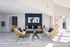 Chic living room with modern decor, featuring cozy wicker chairs, a stylish gray sofa, a glass coffee table, and vibrant artwork against a deep blue accent wall.