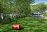 Lush green dog park surrounded by trees, complete with agility equipment and a cozy pavilion.