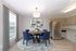 Modern dining area with round wooden table, stylish blue chairs, and contemporary kitchen featuring stainless steel appliances.