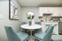 Chic dining nook featuring modern white cabinetry, a sleek round table, and stylish teal chairs, perfect for cozy gatherings.