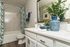 Chic bathroom featuring a marble-patterned shower, elegant white countertop, and stylish blue accents with lush greenery.